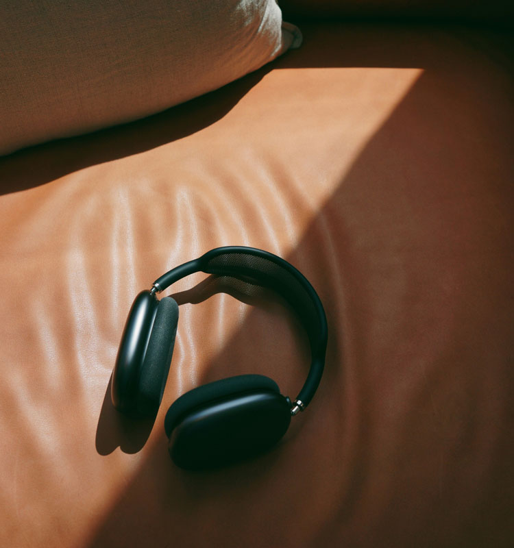 Casque audio posé sur un canapé en cuir camel, éclairé par un rayon de soleil, avec un coussin en tissu clair en arrière-plan.