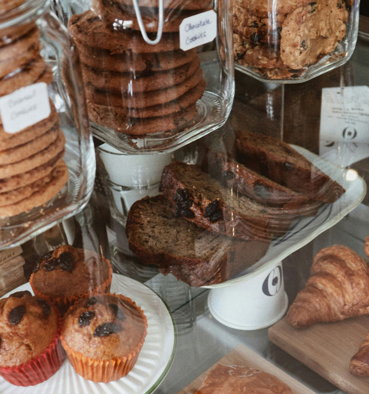 Vitrine garnie de pâtisseries artisanales comprenant cookies, muffins, tranches de cake et viennoiseries, présentées dans des bocaux et assiettes en verre.
