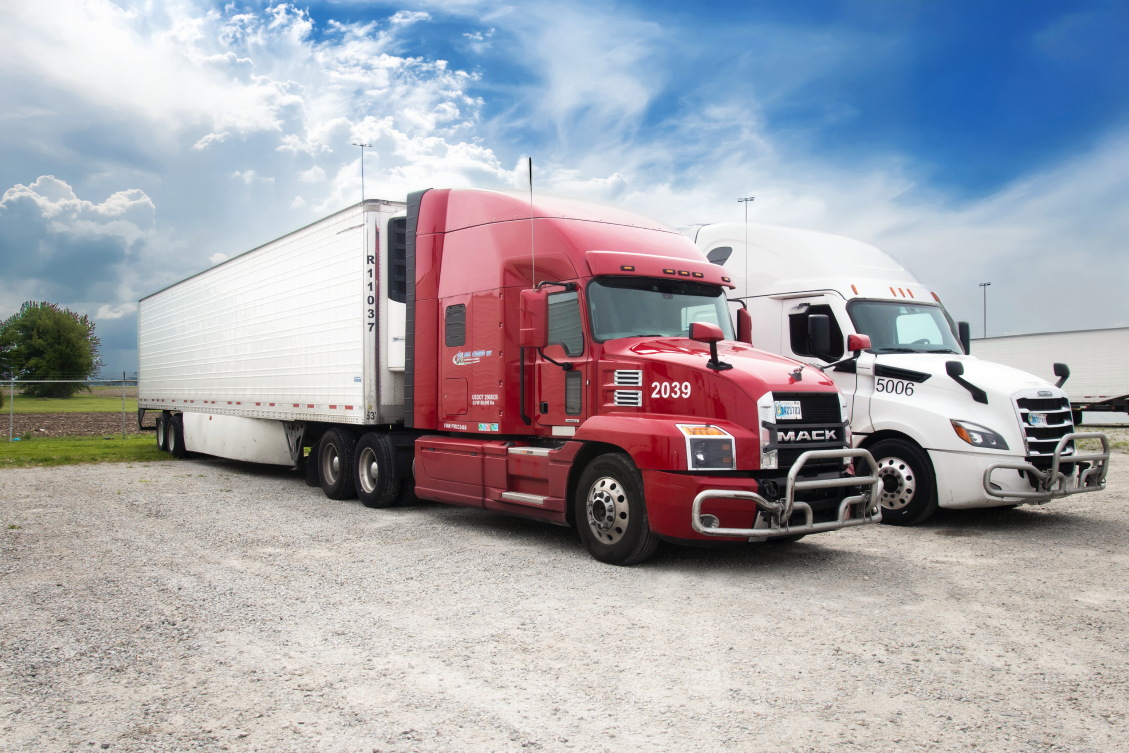 Parked red and white semi trucks with trailers under a partly cloudy blue sky.