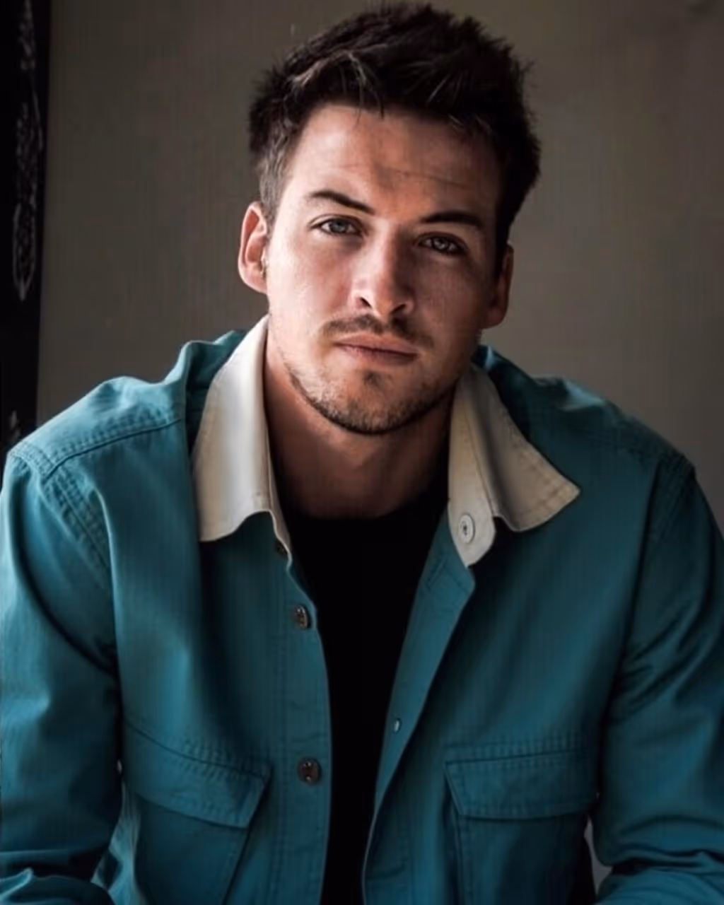 Portrait d'un homme aux cheveux bruns, portant une veste verte avec un col beige clair, regardant directement la caméra.