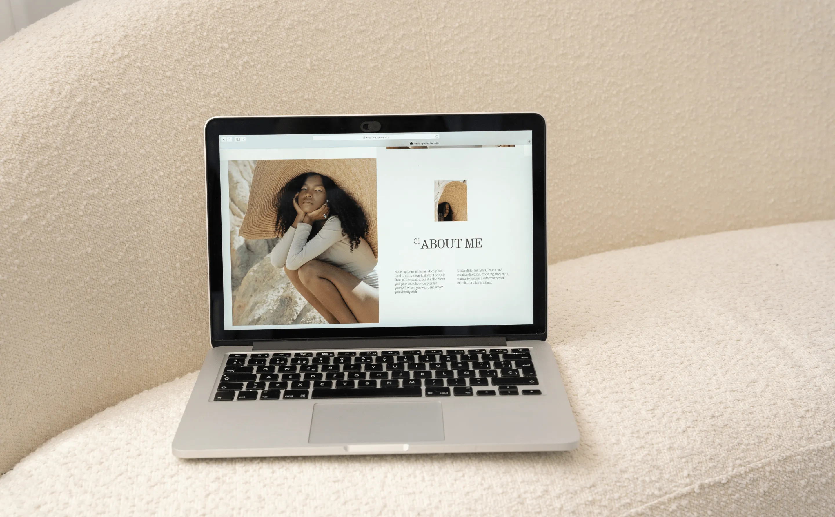Ordinateur portable ouvert affichant une page 'À propos de moi' avec photo d'une femme portant un grand chapeau de paille, posé sur un canapé beige texturé.