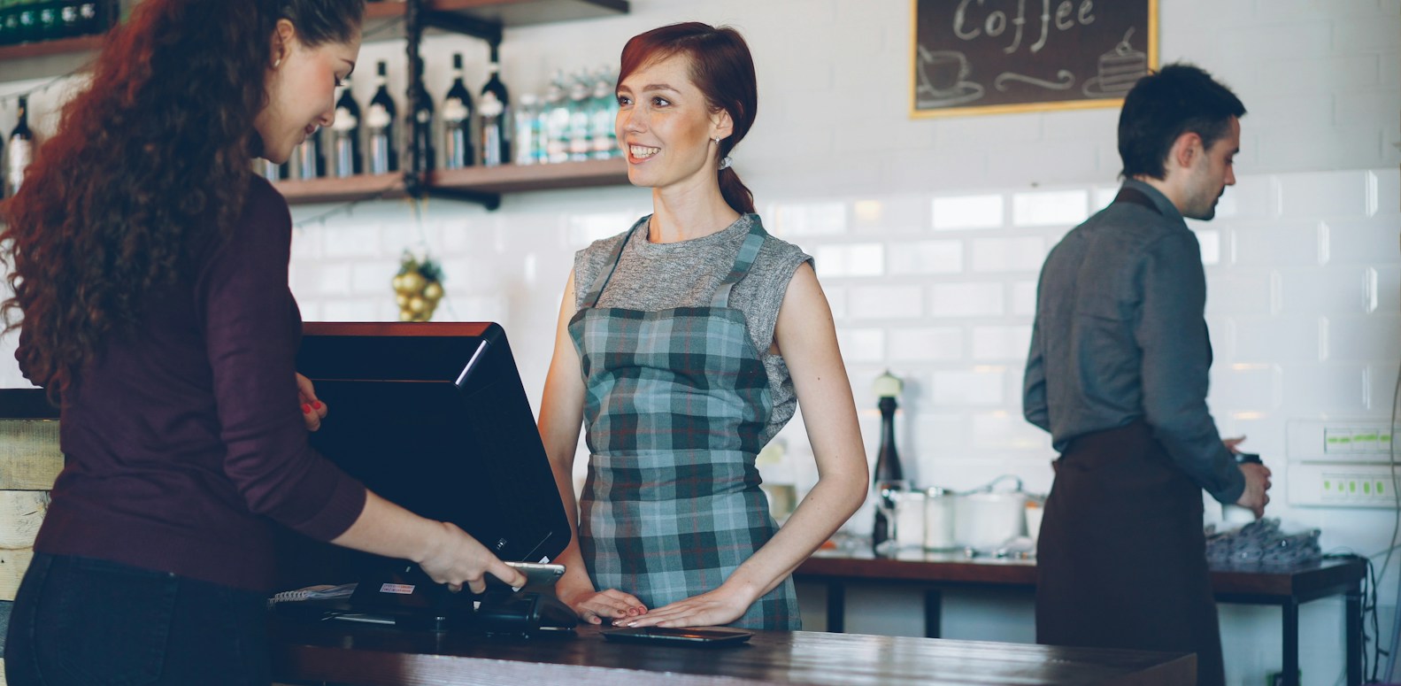 Employés d'un café servant des boissons à emporter pendant que des clients paient avec leur smartphone