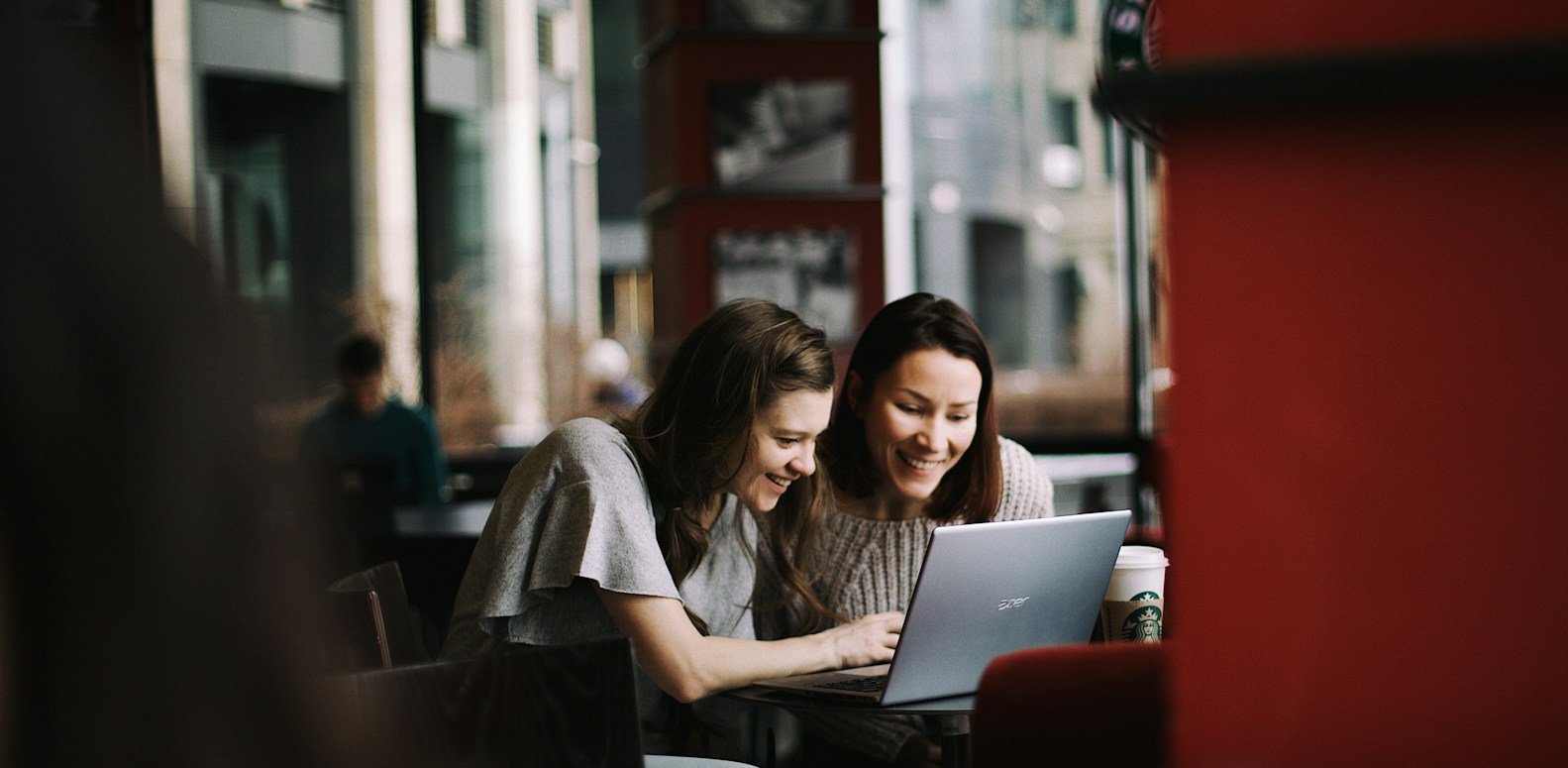 Deux femmes regardent ensemble l'écran d'un ordinateur portable dans un café