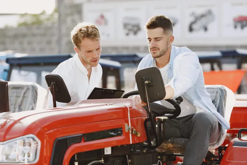 Dealer and customer reviewing details on a tablet beside a tractor