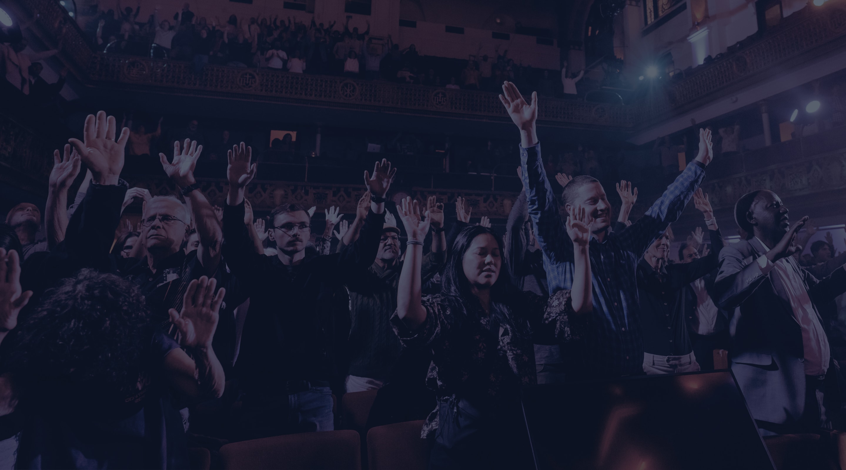 Group of people with hands raised in prayer or worship under bright stage lights during a spiritual or religious gathering.