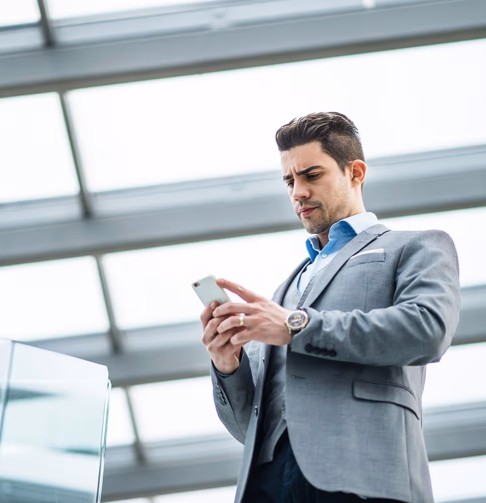 Young businessman in gray suit using smartphone in a bright modern building.