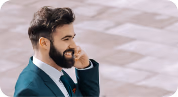 Smiling man in a suit with beard talking on a smartphone outdoors.