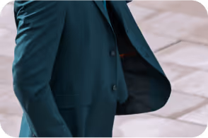 Person wearing a dark teal suit jacket walking on a paved surface.