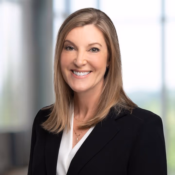Smiling woman with shoulder-length blonde hair wearing black blazer and white blouse.