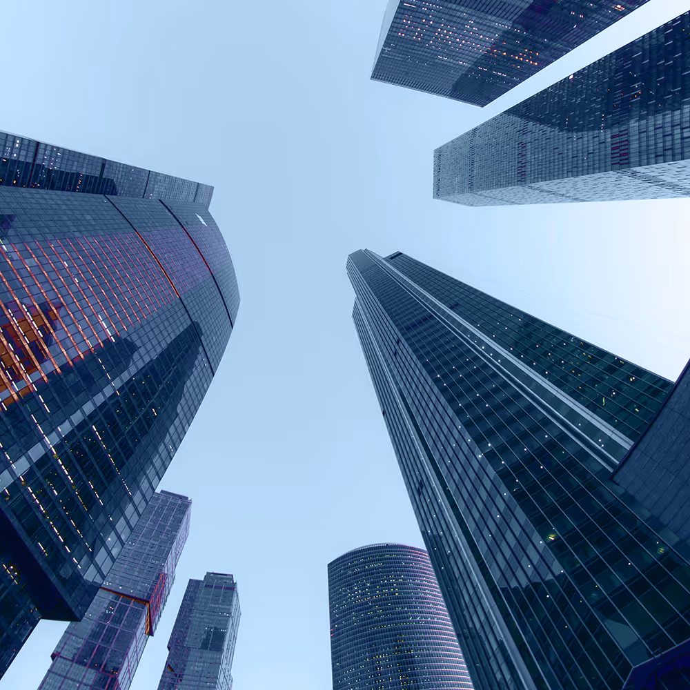 View looking up at tall glass skyscrapers under a clear blue sky in a downtown cityscape.