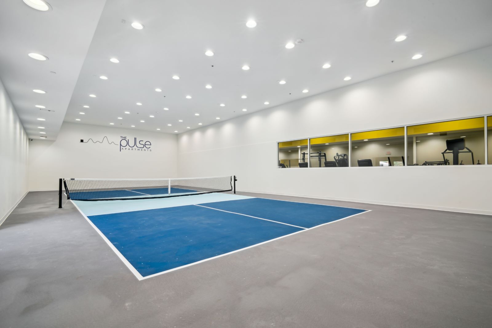 Indoor pickleball court with a net and seating, a unique amenity for residents at The Pulse in Oklahoma City, Oklahoma.