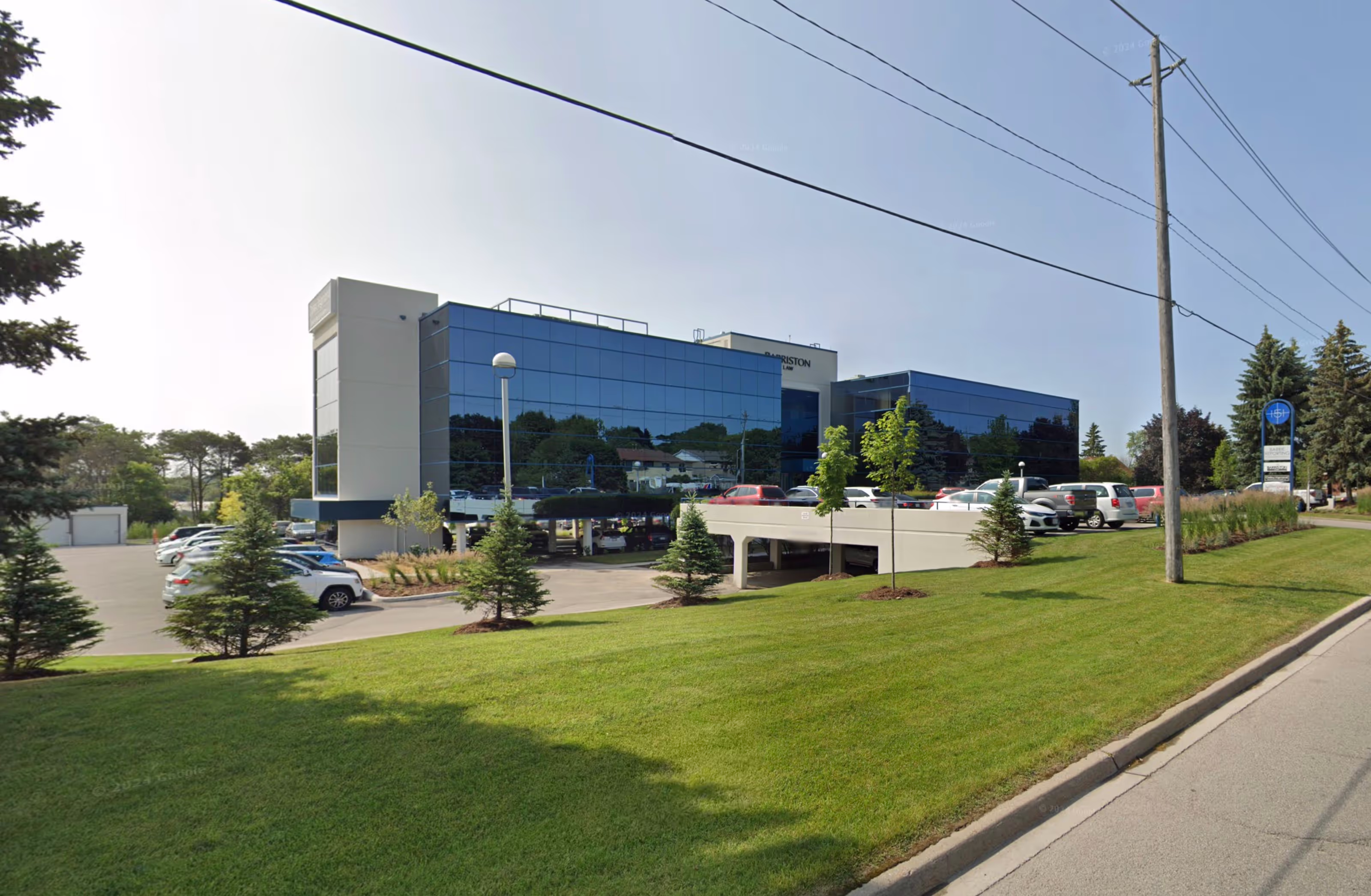 Modern office building with reflective glass exterior, landscaped lawn, and parking area along a main road.
