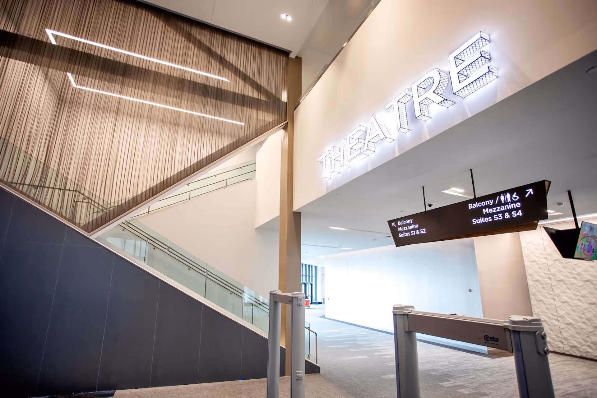 Interior corridor with glass railings and illuminated signage leading to a theatre entrance.