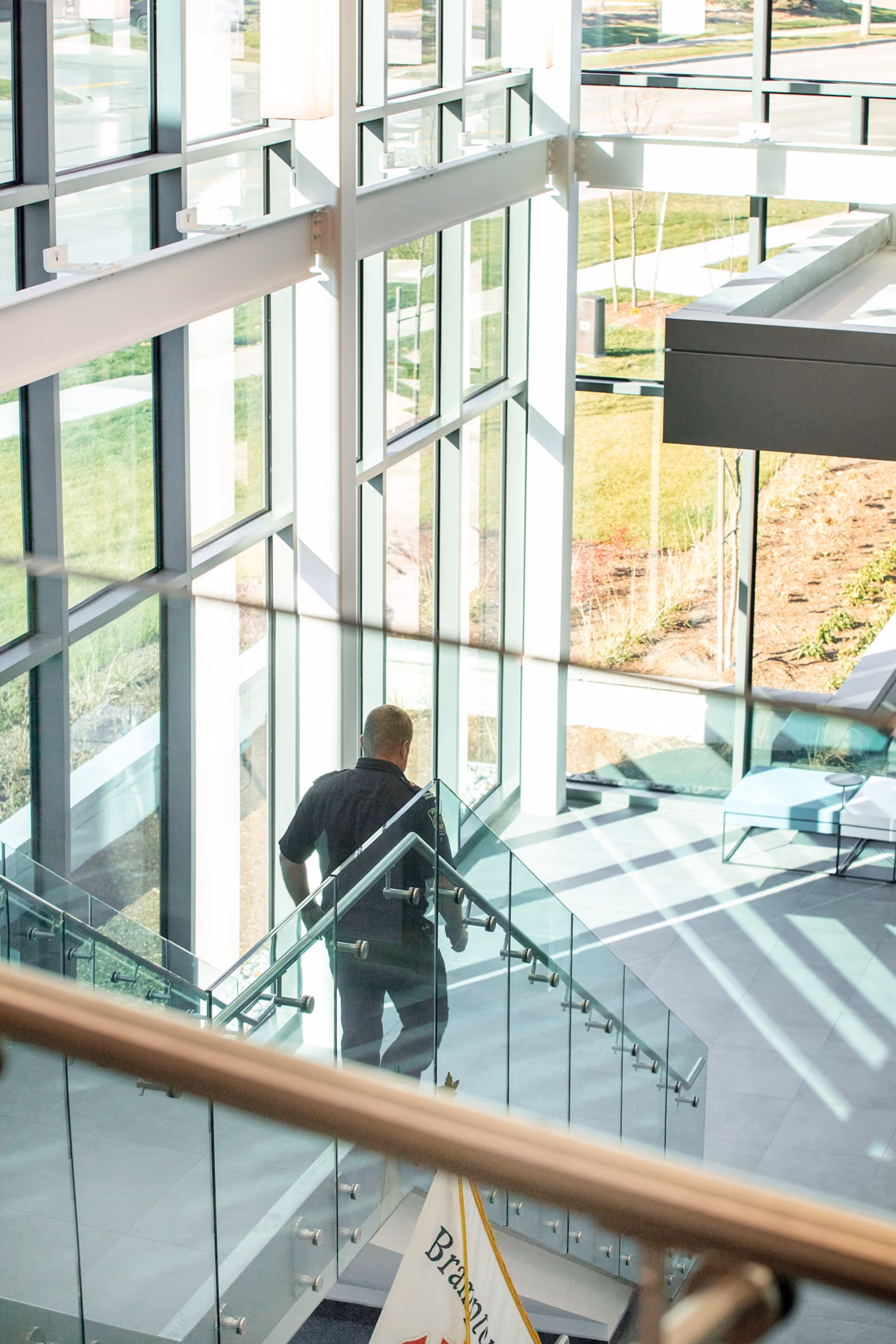 Person walking down a glass staircase inside a bright atrium with large windows and natural light.