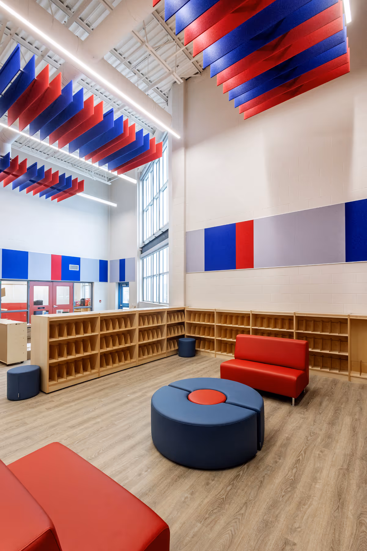 Colorful school interior with red and blue acoustic ceiling panels, wooden cubby shelves, and modern lounge seating.