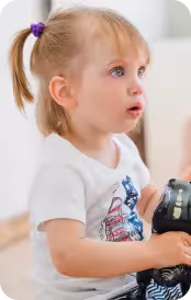 Малко момиче с плитка, държащо черен играчка, гледа надясно с любопитство.