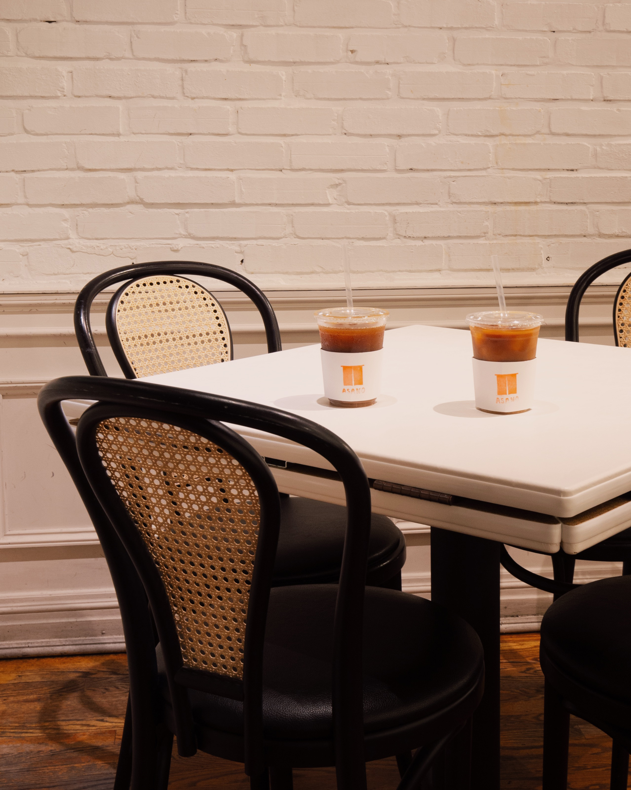 Two iced coffees in ASANO sleeves on a white table with cane chairs at Sandro's