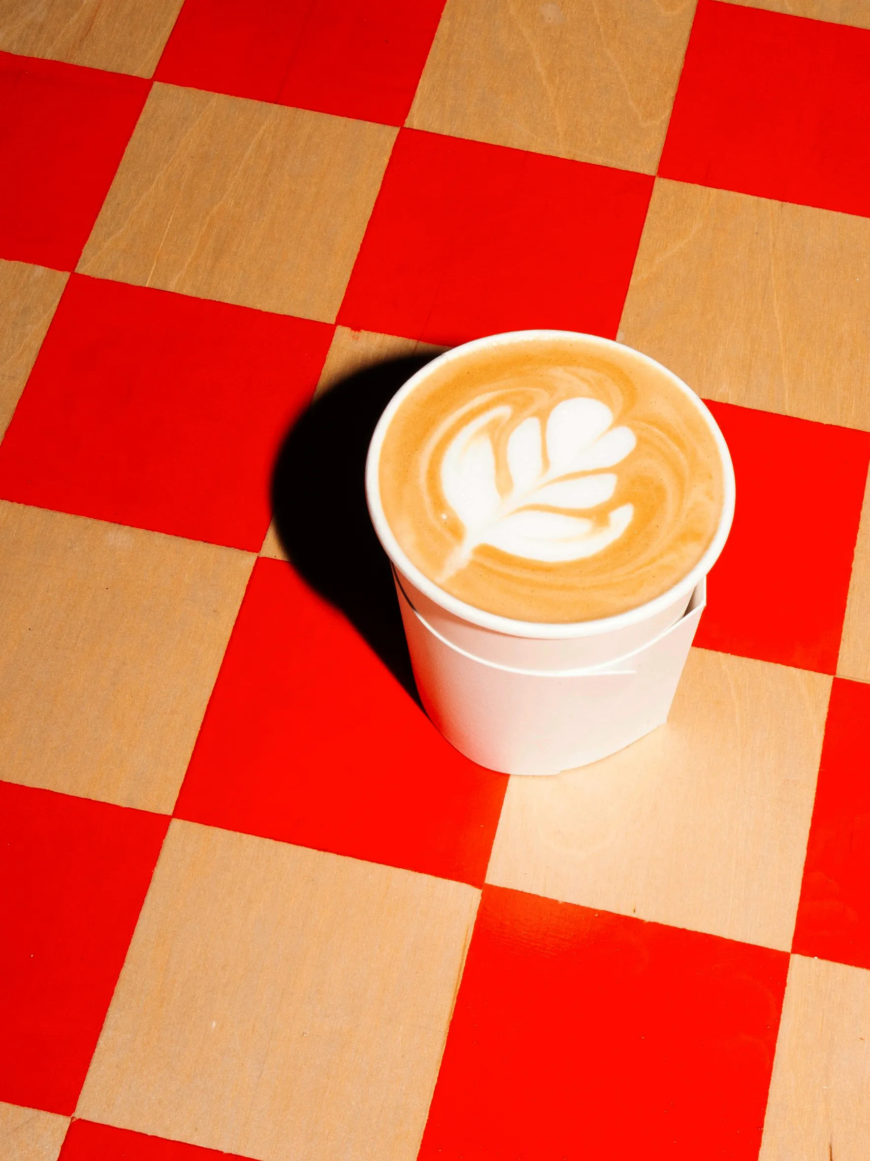 A latte with rosetta latte art in an ASANO cup on a red and natural checkerboard table