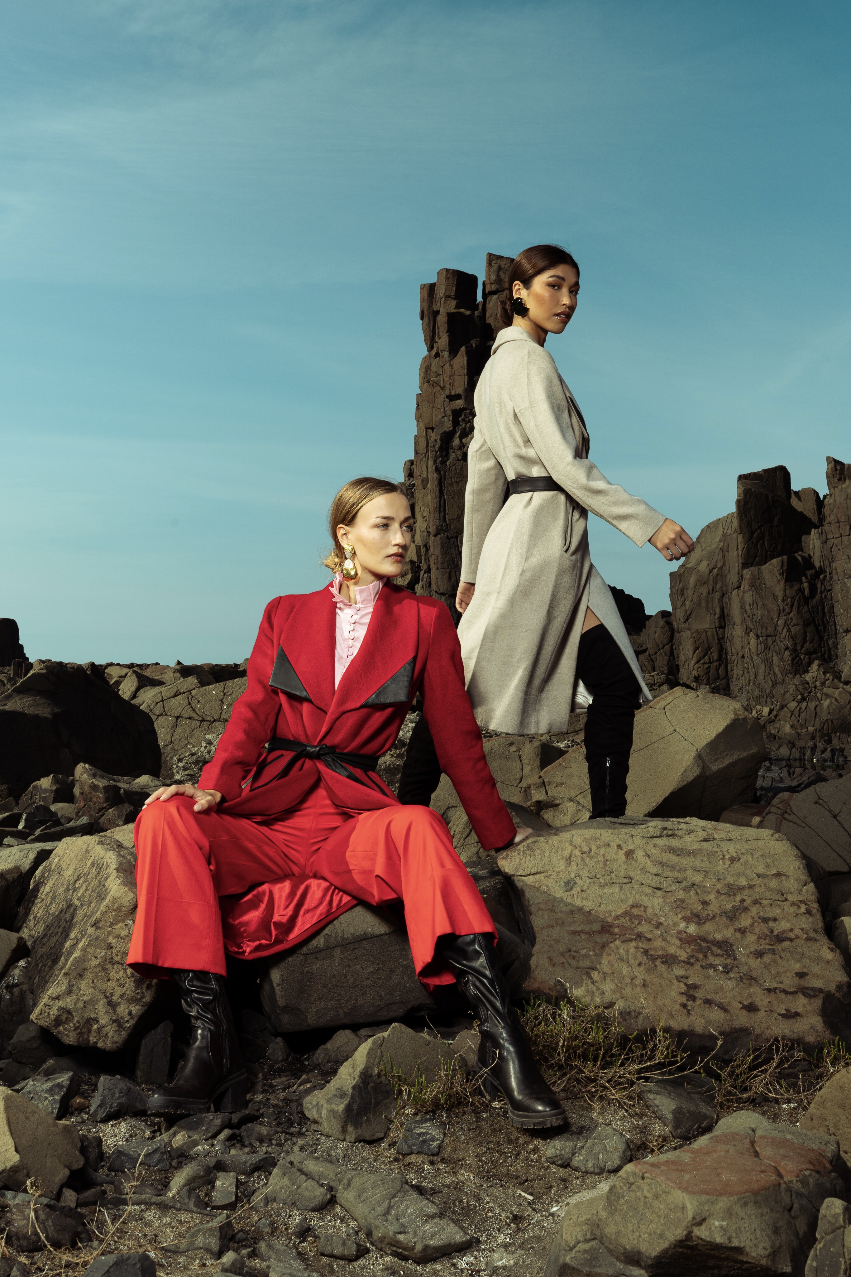 Two models stand poised on the rugged coastline of Sydney, wearing statement wool coats from My Paloma’s winter collection—one in camel beige with a structured belt and the other in bold crimson red with leather accents. Each accessorized with sculptural handbags and silk scarves, epitomizing modern elegance in an editorial worthy of Milan Fashion Week.