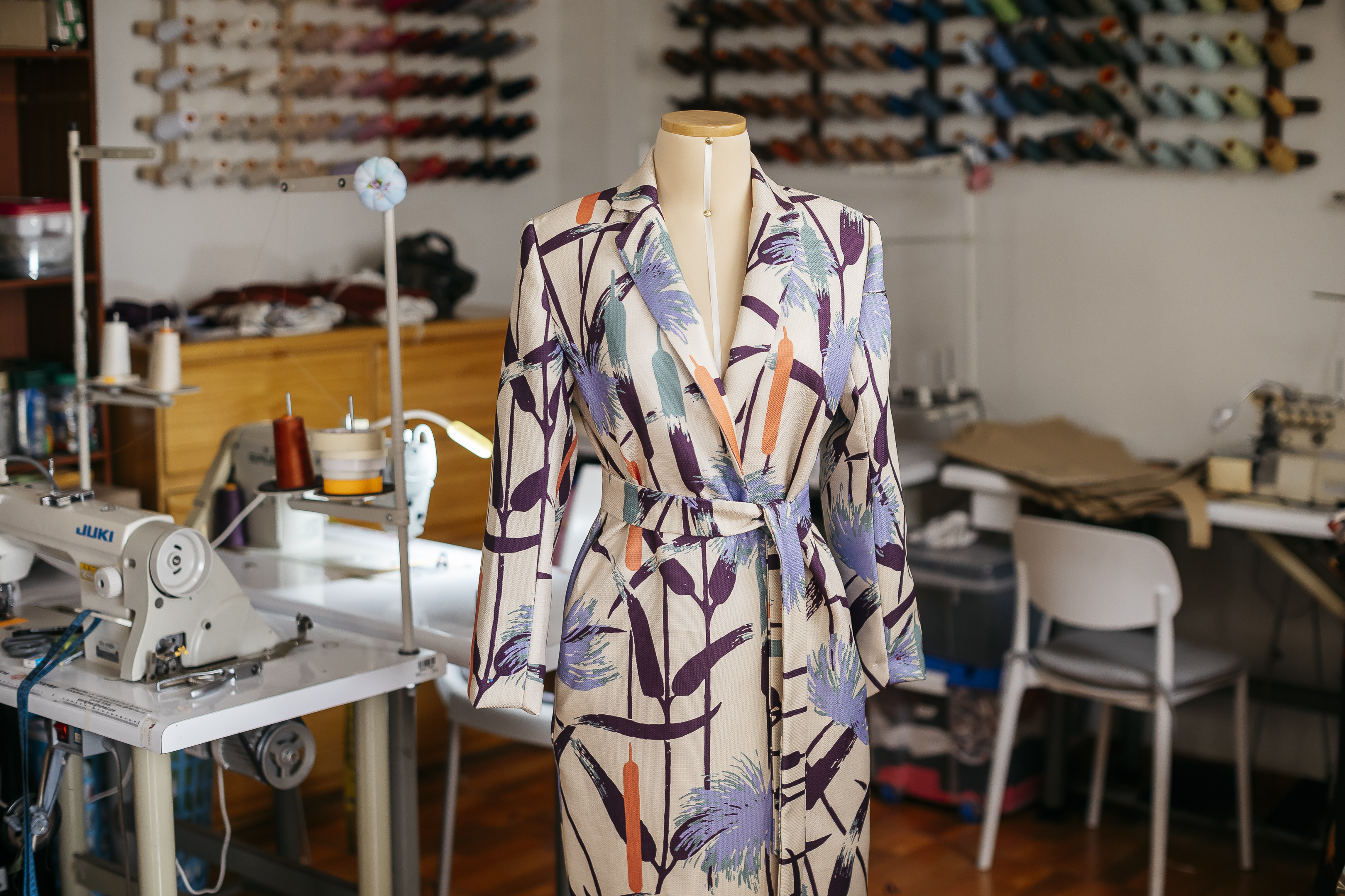 Close-up of model in My Paloma’s signature printed coat with metallic waist belt and gold statement earrings. Styled with a wide teal hat and bold coral eye shadow, this runway-ready ensemble evokes the art-meets-fashion tone of New York and Mexico City’s high-end creative circles.