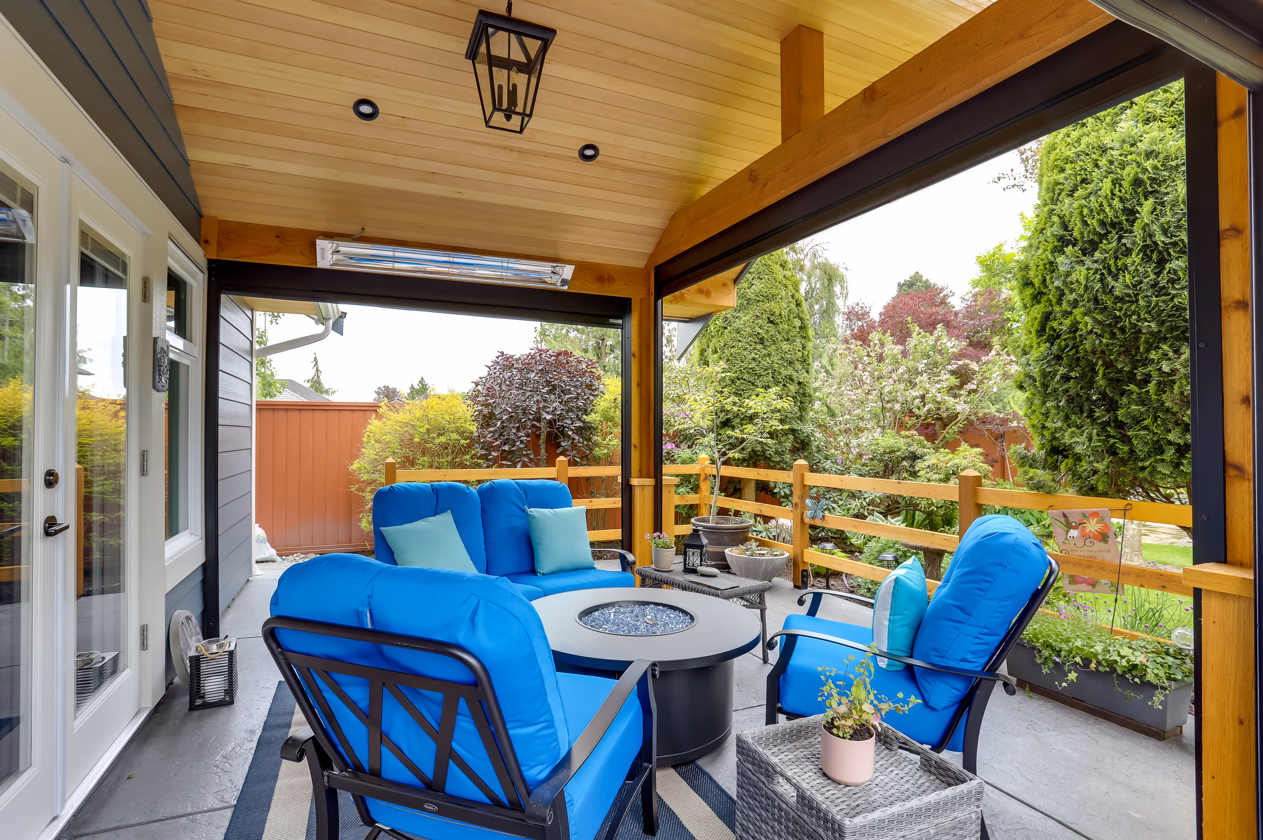 Cozy covered patio with blue furniture, fire pit, and lush garden view