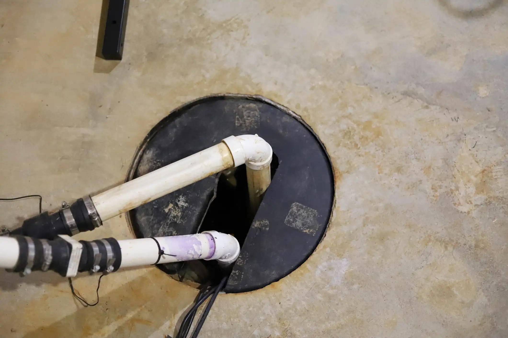 A close-up, overhead view of pipes leading into a sump pump basin in a basement.
