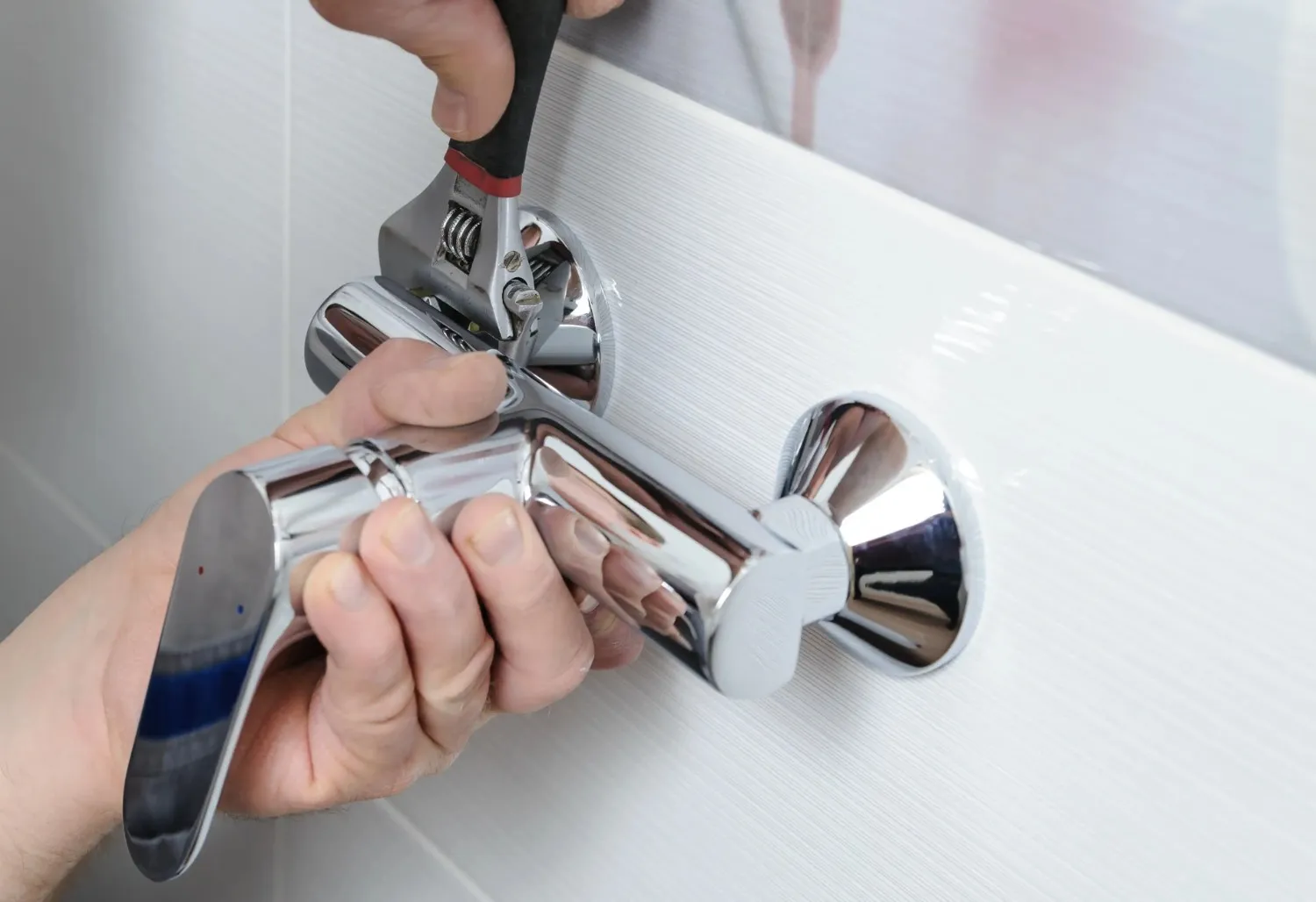 Close-up of a person using a wrench to install a new chrome faucet in a bathroom.