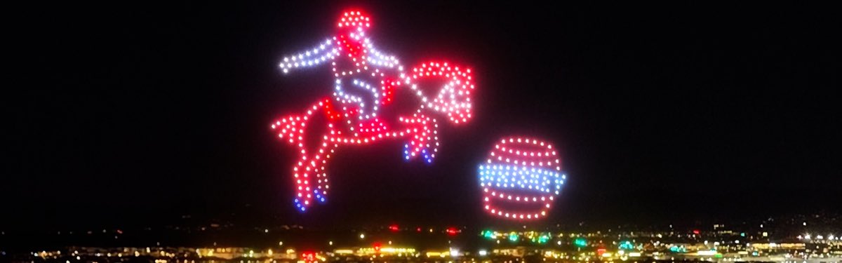 Cowboy riding a bucking horse, drawn in drones above a town at night