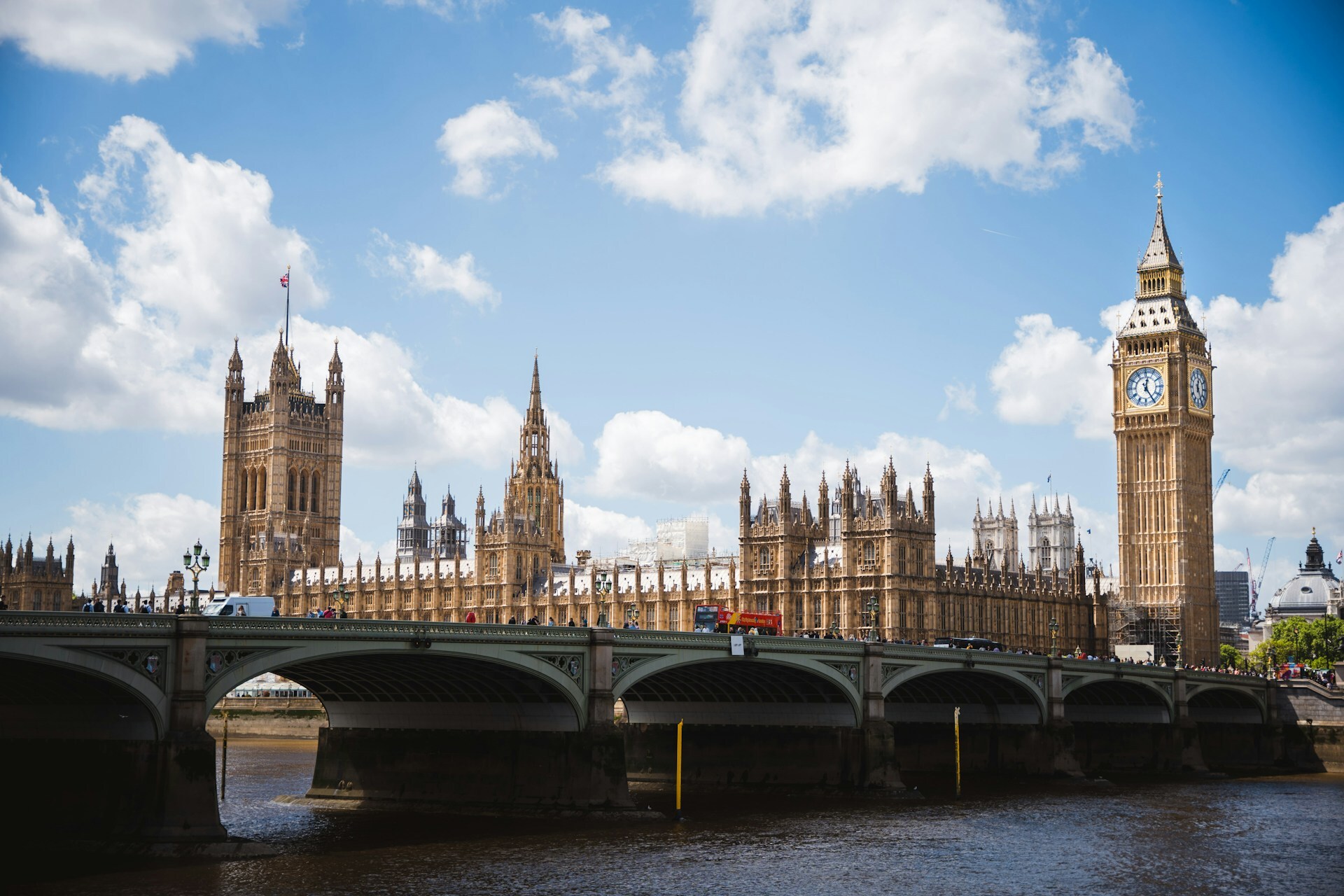 Big Ben and the London Eye under a cloudy sky, with people walking and waiting at a crosswalk. The vibe is busy and iconic London.