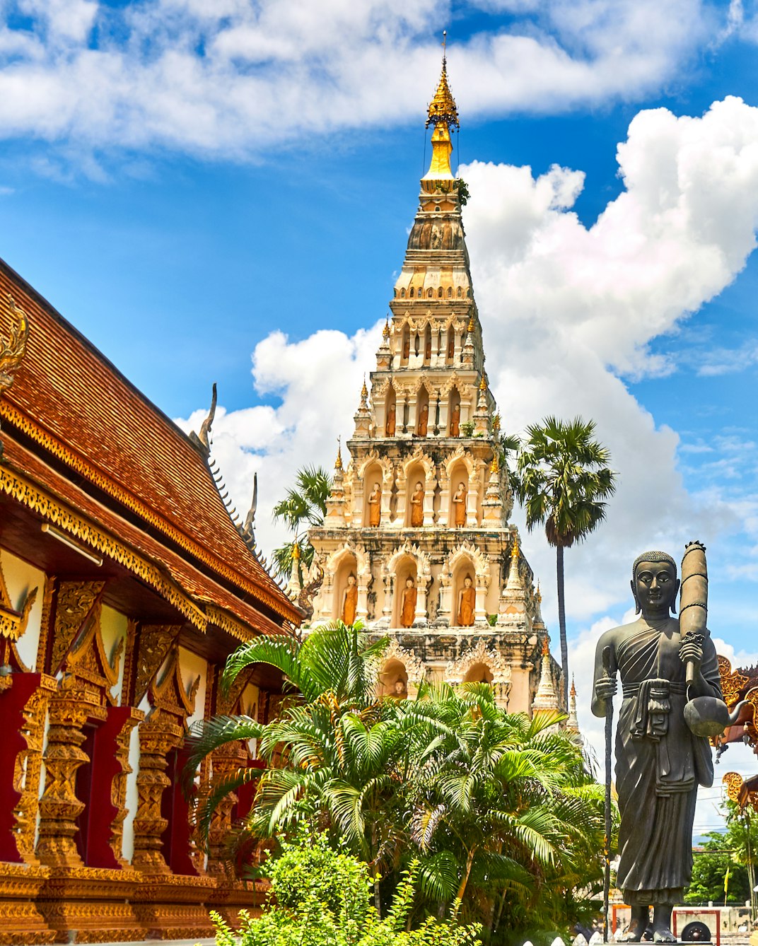 Ornate golden Thai temple buildings and palm trees under a blue sky.