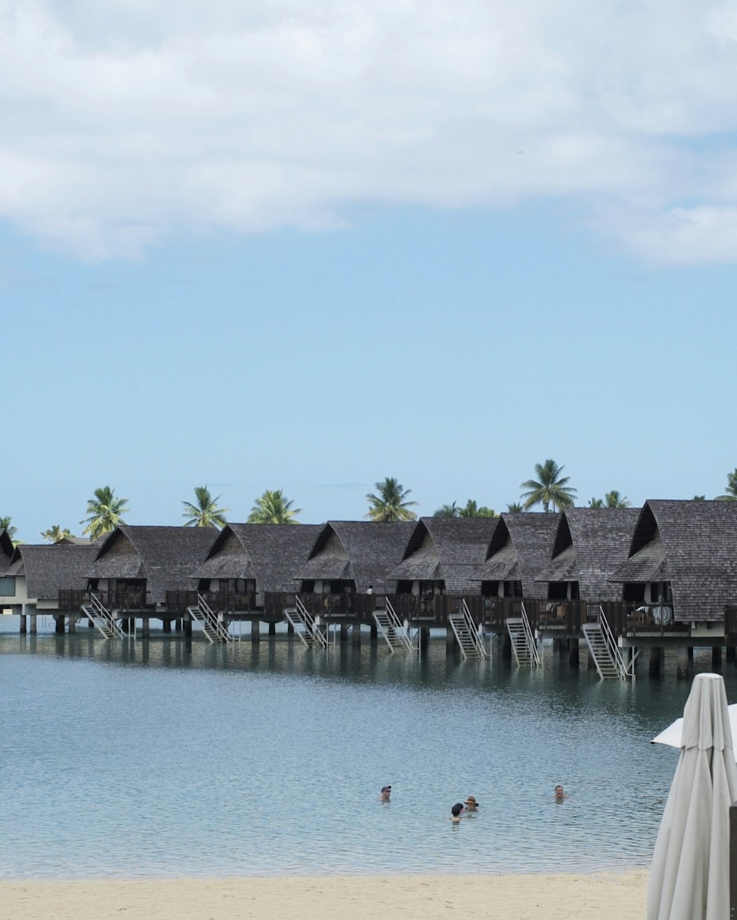 A row of thatched overwater bungalows on calm turquoise water at a Fiji island resort.
