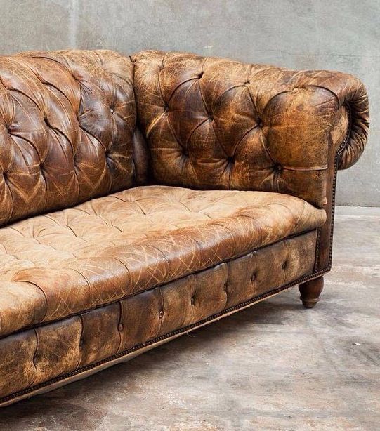 Worn brown tufted leather sofa with visible fading, scratches, and creasing