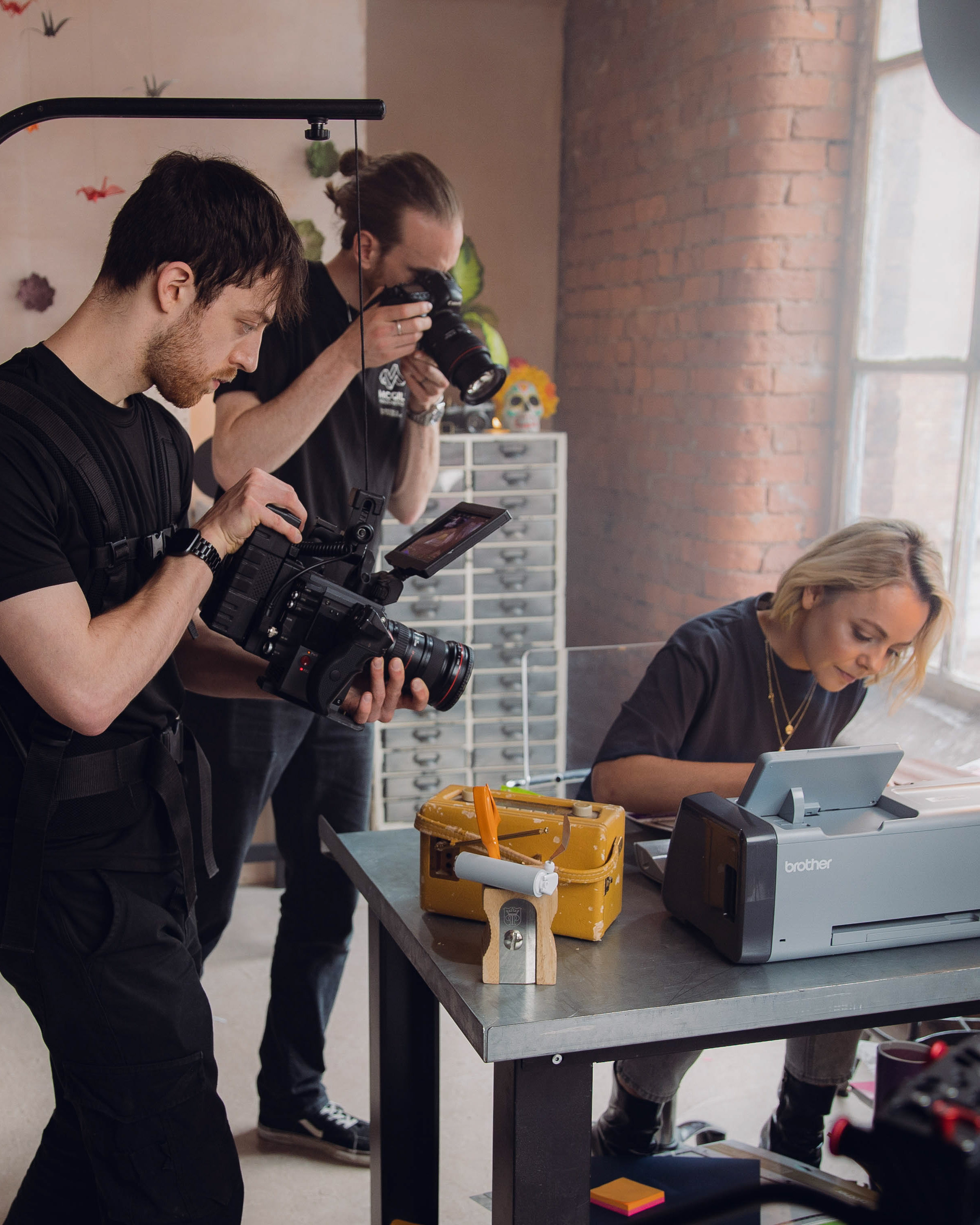 A videographer and a photographer can be seen capturing a woman using a Brother machine. On set of a Brother product promo video.