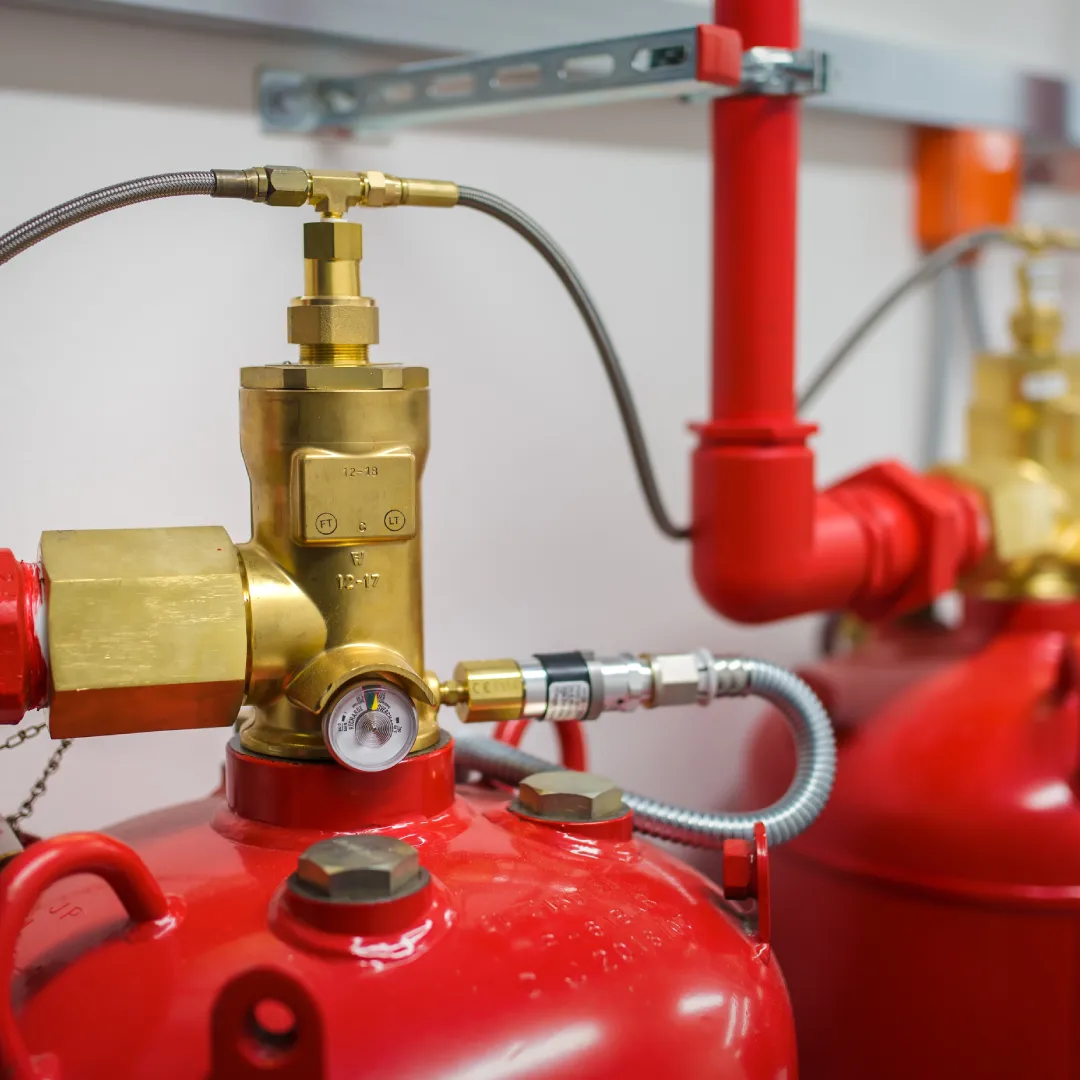 Close-up of a red fire suppression cylinder with a brass valve and pressure gauge attached.