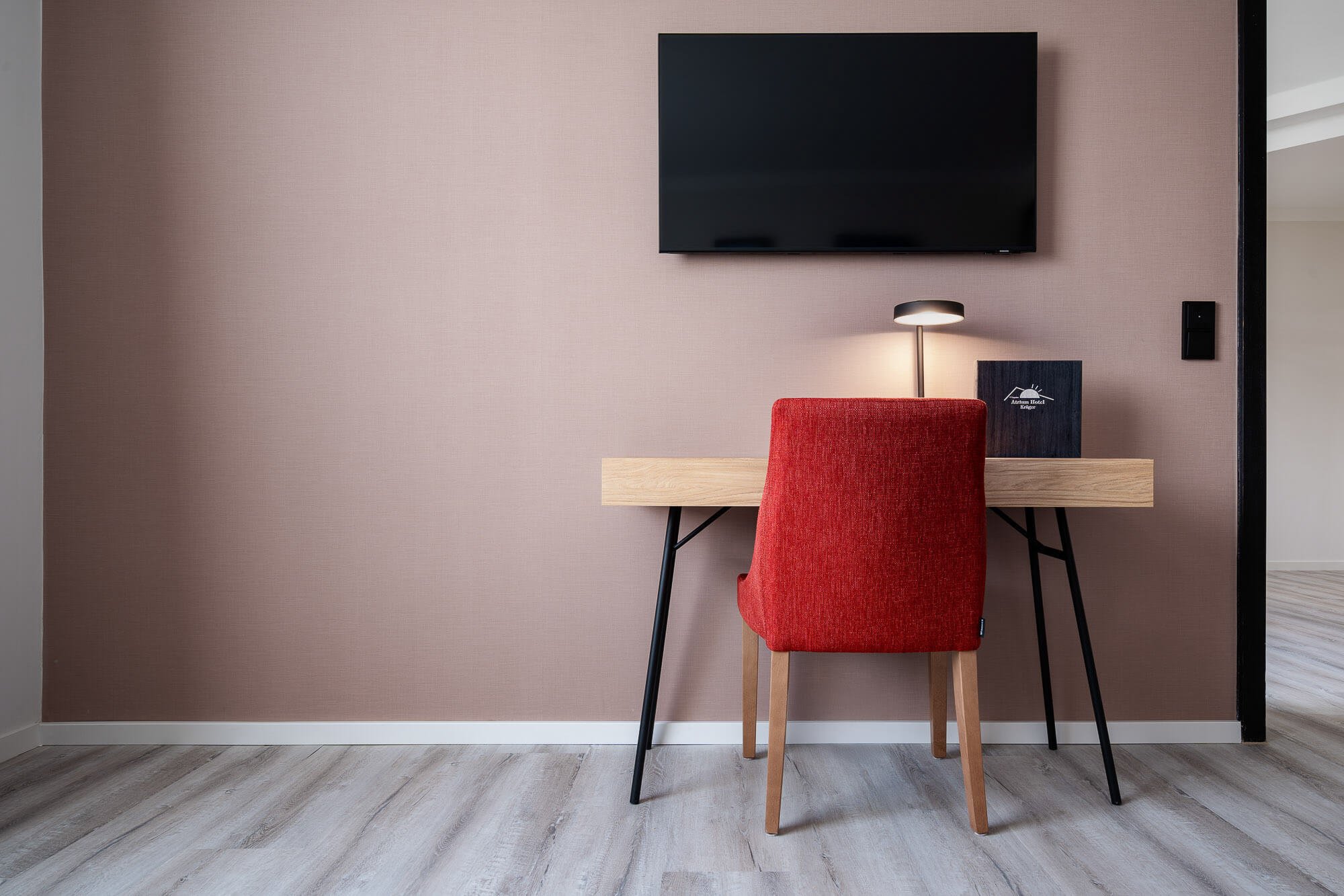 Schreibtisch mit rotem Stuhl unter Wandbildschirm im Hotelzimmer