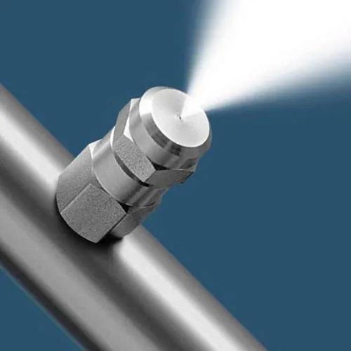 Metal nozzle attached to pipe spraying a fine mist of liquid against blue background.