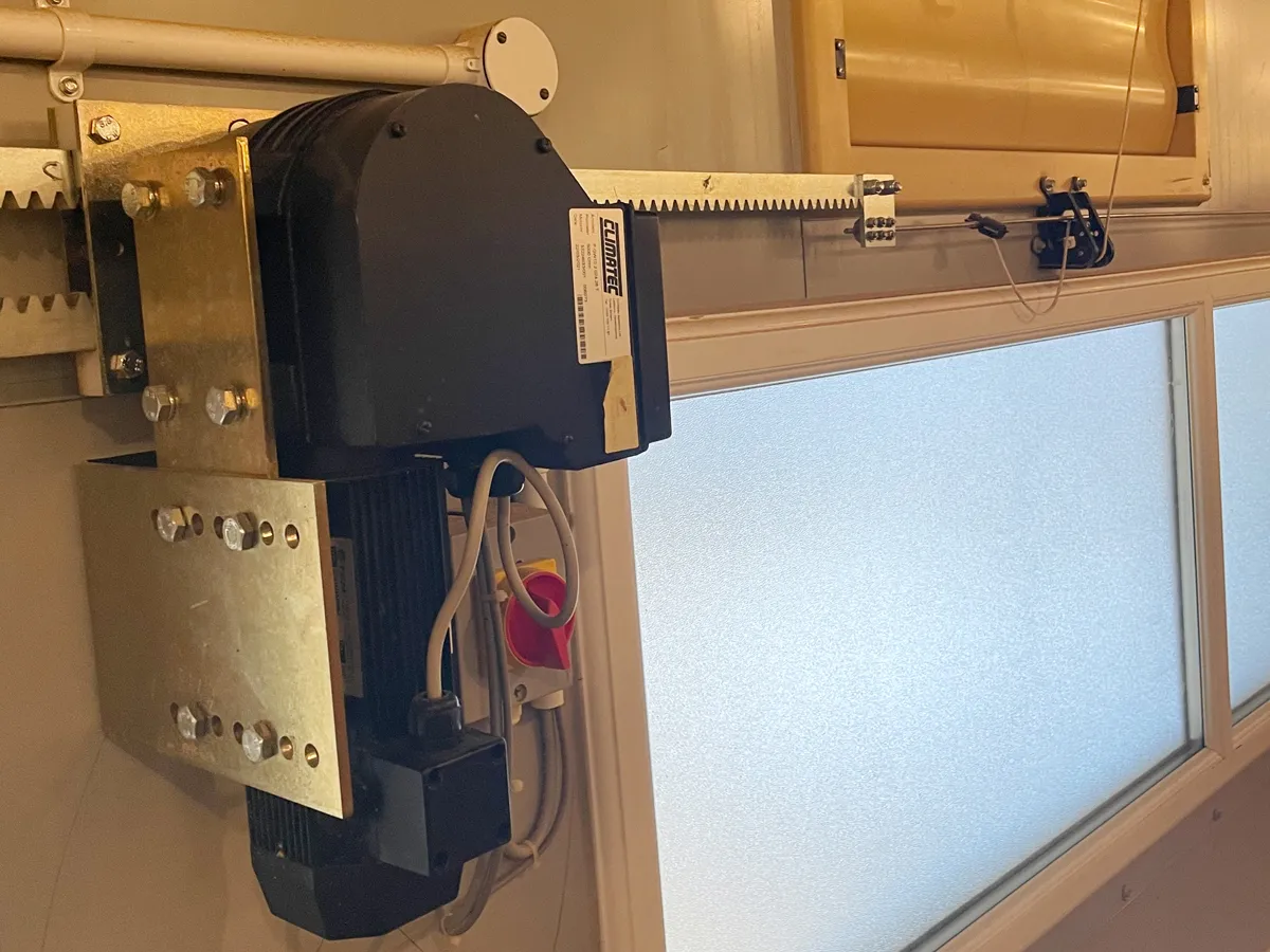 Close-up of a black electric garage door motor unit mounted with metal brackets next to a frosted window.