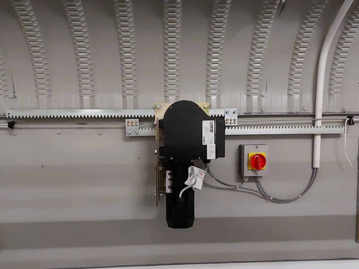 Electric garage door motor mounted on a wall with metal rack and a red power switch box.