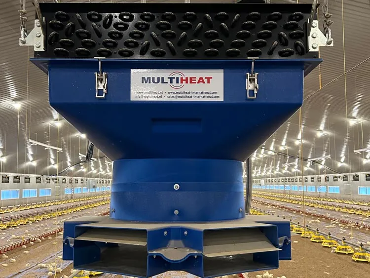 Blue automated poultry feeder with black feed pellets inside in a large indoor chicken farm.