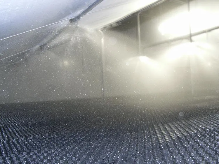 Spray mist from nozzles inside an industrial air scrubber system with a textured grid floor.