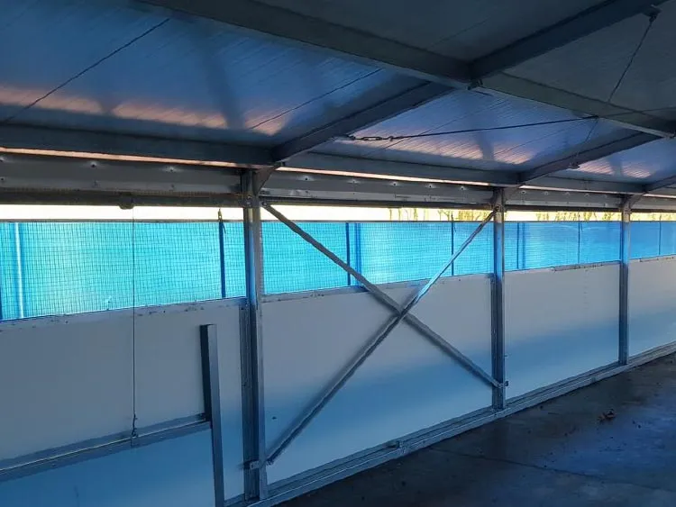 Interior of a metal-framed shelter with blue tarp panels and white lower walls.