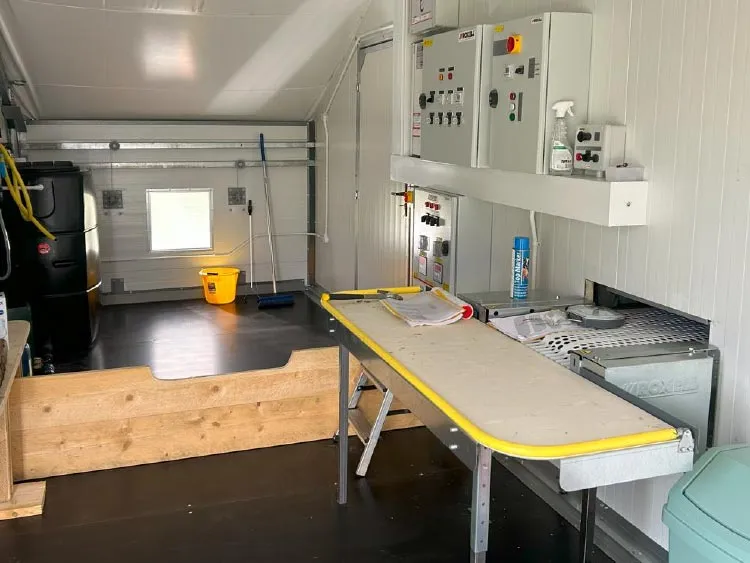 Interior of a utility shed with control panels, a table with tools and papers, cleaning supplies, and a small window.