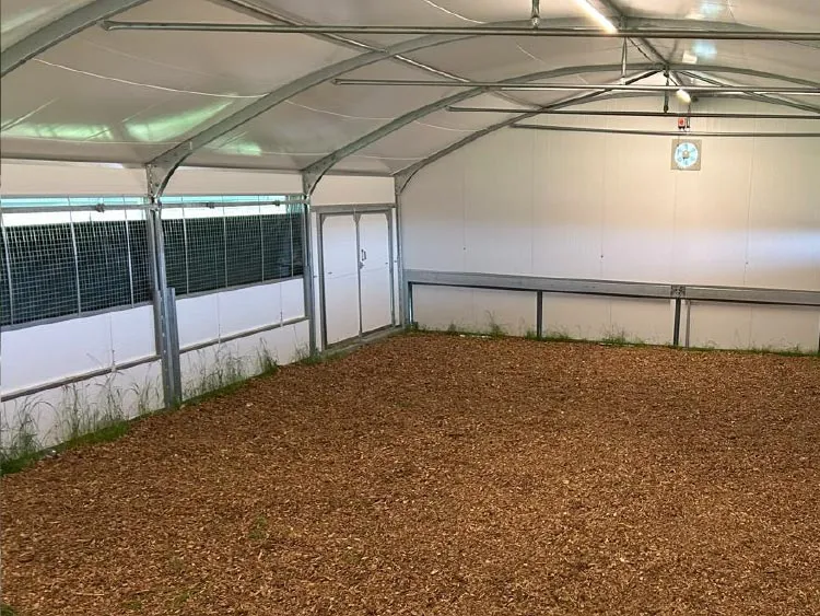 Interior of a metal-framed shed with wood chip flooring and white panel walls under a curved roof.