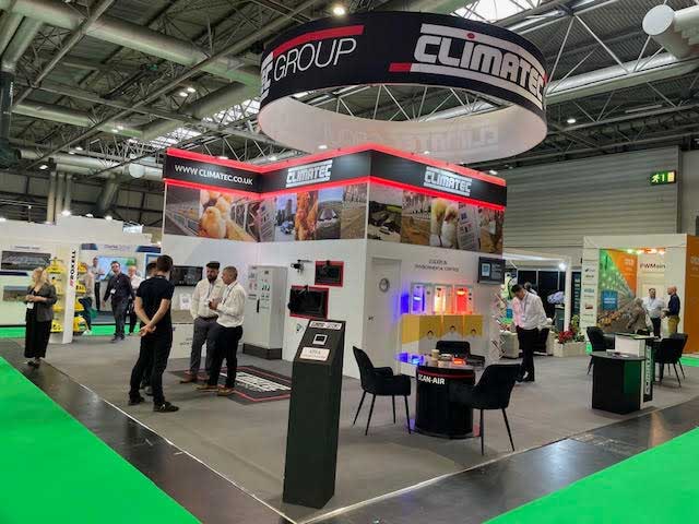 Exhibition booth for Climatec with company branding, display screens, and people conversing inside a convention center.