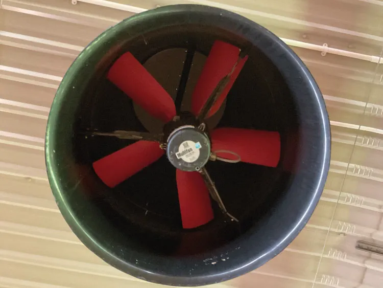 Large industrial ventilation fan with red blades mounted on a beige ceiling.