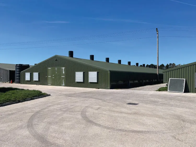 Large green agricultural shed with ventilation vents under a clear blue sky.