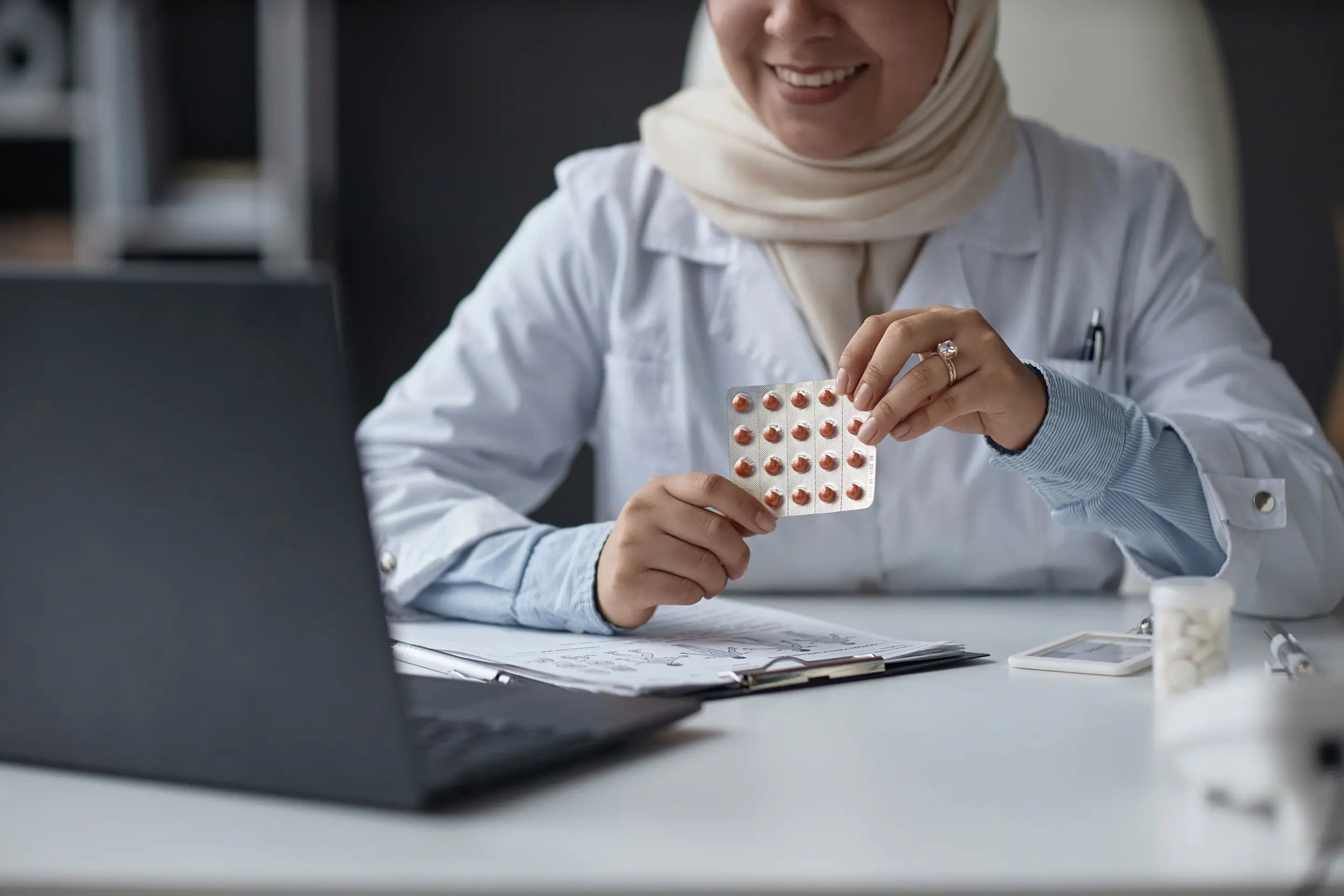 A doctor showing prescription pills in front of her laptop in office