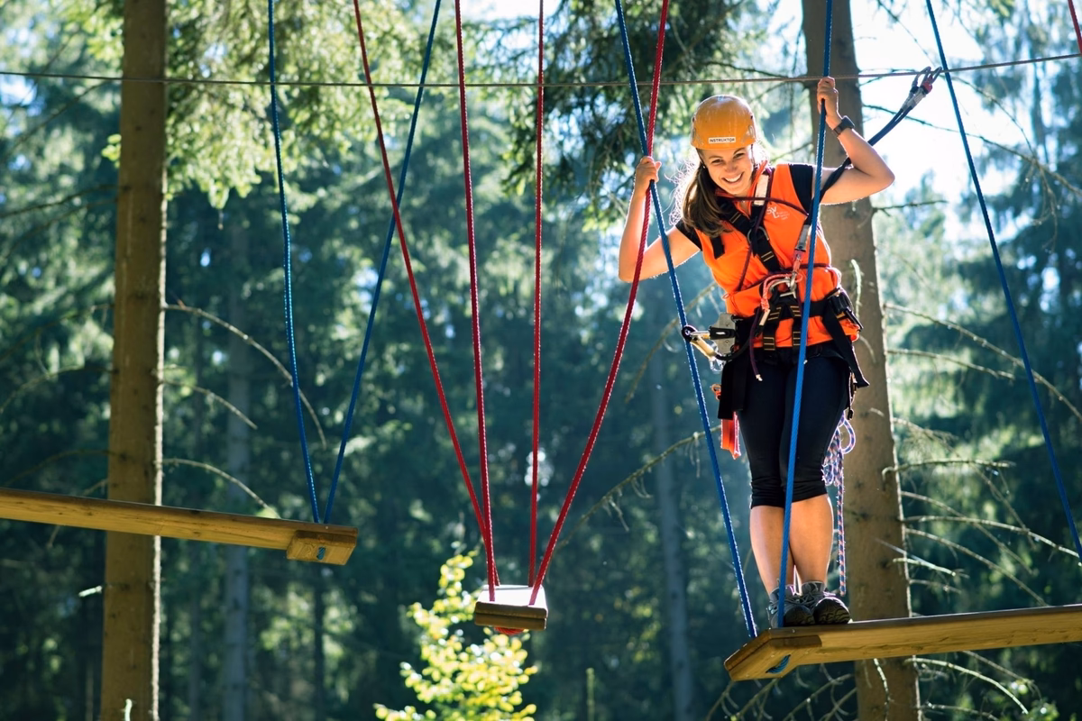 Woman in a harness and helmet crossing a rope course obstacle in a forest