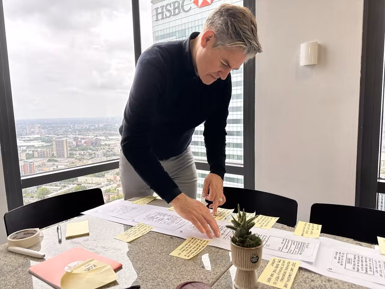 Facilitator Rob Hamblen assembling parts of his Design Sprint concept sketch in a London office with the HSBC building behind him.