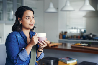 A person holding a mug and looking out a window in a kitchen.